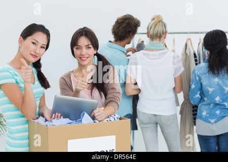 Persone con vestiti di donazione e tavoletta digitale gesticolando pollice in alto Foto Stock