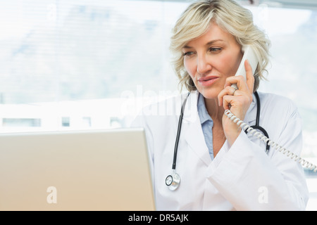 Medico utilizzando laptop e telefono in ufficio medico Foto Stock