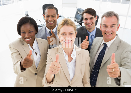 Chiudere diversi team aziendale sorridente fino a telecamera dando pollice in alto Foto Stock