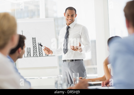 Felice giovane impreditore presentando grafico a barre a co lavoratori Foto Stock