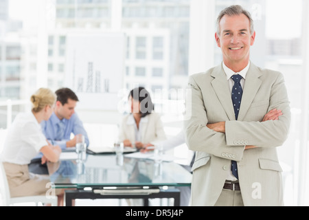 Happy businessman guardando la fotocamera mentre il personale discutere dietro di lui Foto Stock