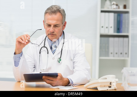 Focalizzato medico seduto alla sua scrivania con clipboard Foto Stock