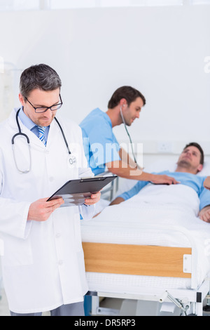 Medico scrivere rapporti con il paziente ed il chirurgo in background Foto Stock