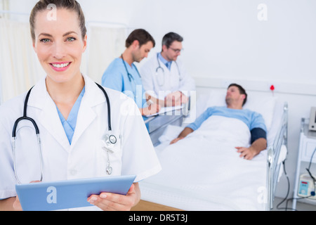 Medico usando tavoletta digitale con i colleghi e il paziente dietro Foto Stock