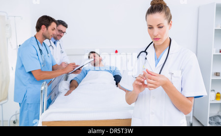 Medico tenendo una siringa con i colleghi e il paziente in ospedale Foto Stock