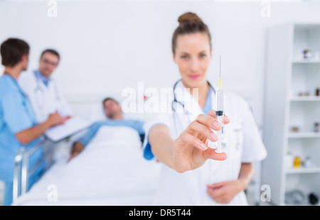 Medico tenendo la siringa con i colleghi e il paziente in ospedale Foto Stock