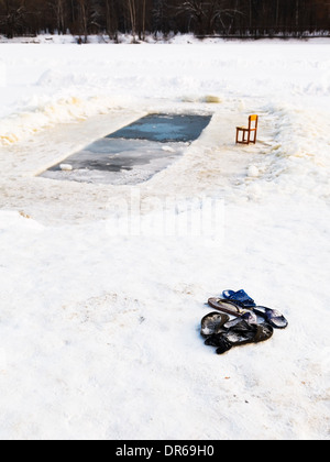 Pantofole e una sedia vicino al foro di ghiaccio nel lago ghiacciato in inverno freddo giorno Foto Stock