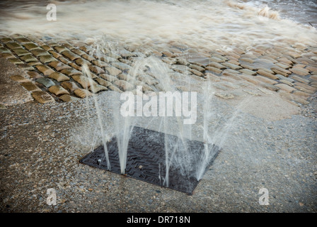 Lo scoppio di acqua da un pozzo in strada durante gravi inondazioni. Foto Stock