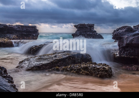 L'oceano cascading su rocce esposte affiorante all alba alla spiaggia sabbiosa di Oahu, Hawaii Foto Stock