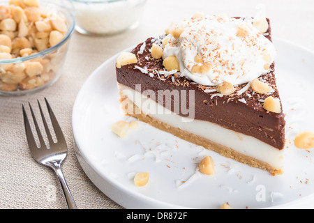 Haupia decadente e crema al cioccolato torta guarnita con radere noce di cocco, noci di macadamia e scaglie di cioccolato con panna montata Foto Stock
