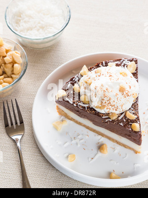 Haupia decadente e crema al cioccolato torta guarnita con radere noce di cocco, noci di macadamia e scaglie di cioccolato con panna montata Foto Stock
