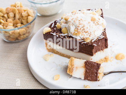 Haupia decadente e crema al cioccolato torta guarnita con radere noce di cocco, noci di macadamia e scaglie di cioccolato con panna montata Foto Stock