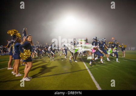 Alta scuola calcio football giocatori corrono attraverso un inspirational banner detenute da cheerleader all'inizio di un gioco di notte a San Juan Capistrano, CA. Foto Stock