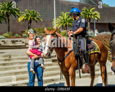 Nella sua madre bracci, una bambina incontra un amichevole montato funzionario di polizia di cavallo in San Francisco Golden Gate Park. Nota DeYoung Art Museum in background. Foto Stock