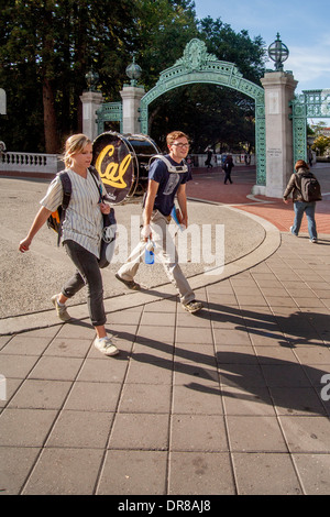 Accompagnata da una donna un compagno di college band musicista porta un bass drum passato Sather cancello sul campus della University of California a Berkeley. Nota Cal logo sul tamburo. Foto Stock