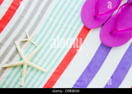Spiaggia scena con viola flip flop e due stelle marine su una spiaggia a strisce asciugamano. Foto Stock