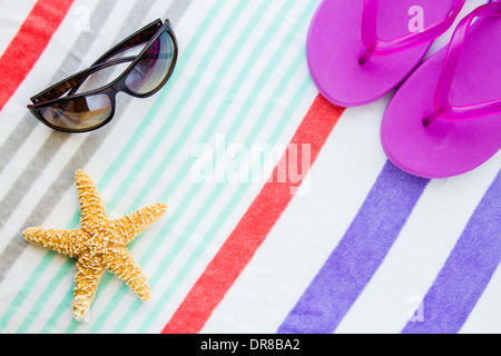 Spiaggia scena con viola infradito, occhiali da sole e una stella di mare su una spiaggia a strisce asciugamano. Foto Stock