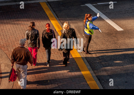 Un americano asiatico police officer dirige il traffico sul campus della University of California a Irvine. Nota luminosa luce del mattino e visibilità abbigliamento di sicurezza. Nota pedoni che attraversano street. Foto Stock