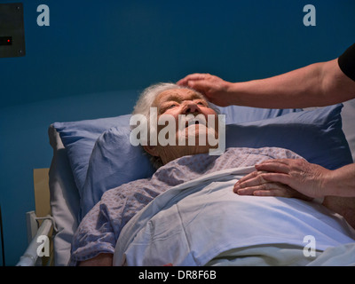 Felice sorridente senior età anziana signora nel letto di ospedale con mano confortante del caregiver infermiere Foto Stock