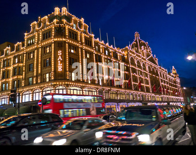 I grandi magazzini Harrods al crepuscolo con accesa 'sale' firmare gli acquirenti bus rosso passando i taxi e limousine stretch Knightsbridge London SW1 Foto Stock