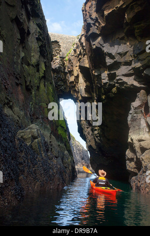 Sea kayaker paddling attraverso un arco su Rathlin O'Birne Isola, County Donegal, Irlanda. Foto Stock