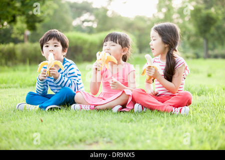 I bambini seduti sull'erba mangiando le banane Foto Stock