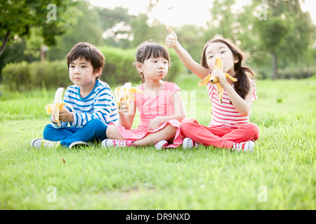 I bambini seduti sull'erba mangiando le banane Foto Stock