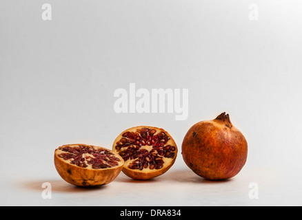 Due melagrane su uno sfondo bianco illuminato laterale da destra e uno tagliato a metà per rivelare il rosso semi commestibili di frutta Foto Stock