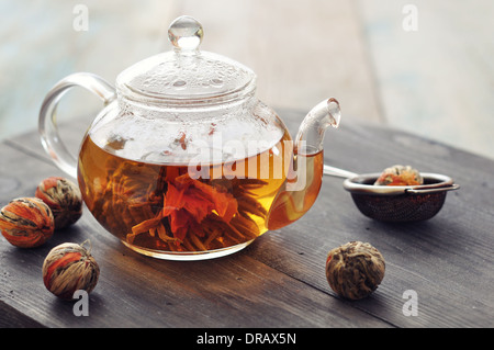 Fioritura cinese tè nella teiera in vetro su sfondo di legno Foto Stock