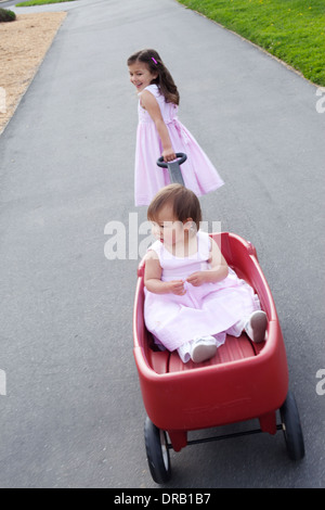 Sorella maggiore tirando la sua sorella più giovane in un carro rosso Foto Stock