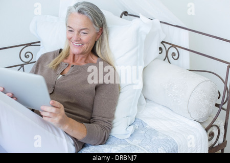 Donna senior con tavoletta digitale sul letto Foto Stock