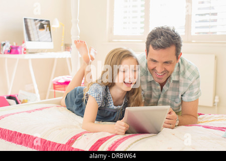 Padre e figlia con tavoletta digitale sul letto Foto Stock