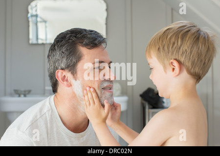 Ragazzo sfregamento crema di rasatura sul volto del padre Foto Stock