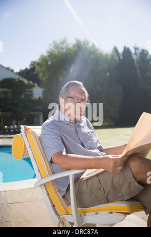 Uomo che legge il giornale a bordo piscina Foto Stock