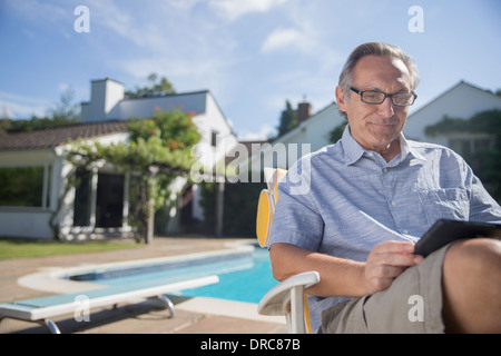 Uomo con tavoletta digitale a bordo piscina Foto Stock