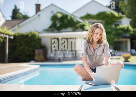 Donna che utilizza computer portatile sulla scheda di immersioni presso la piscina Foto Stock