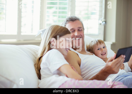 Padre e figli utilizzando digitale compressa sul letto Foto Stock