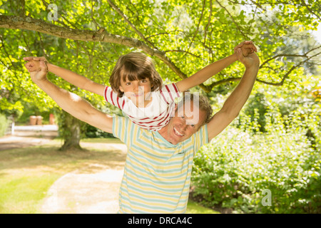 Padre piggybacking figlio sotto agli alberi Foto Stock