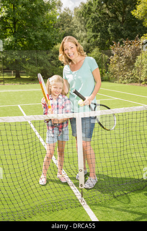 Madre e figlia sorridente sul campo da tennis d'erba Foto Stock