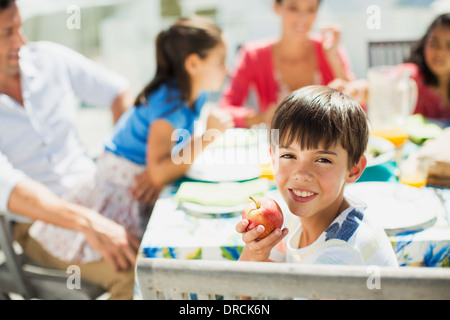 Ragazzo mangiare la frutta con la famiglia a tavola sul patio soleggiato Foto Stock