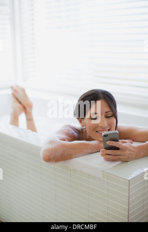 Donna che utilizza il cellulare in vasca da bagno Foto Stock