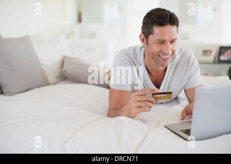 L uomo lo shopping online con il computer portatile sul letto Foto Stock