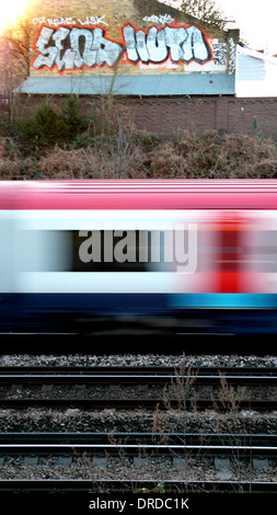 Un treno lampeggia da una coperta di graffiti a parete con la luna nuova in background Foto Stock