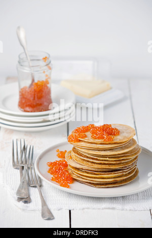 Frittelle con caviale rosso su bianco sullo sfondo di legno Foto Stock