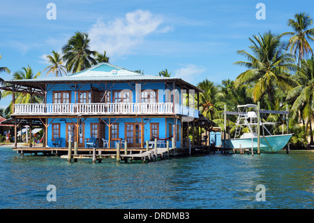 Bellissima casa tropicale su palafitte sopra il mare dei Caraibi con una barca e gli alberi di cocco, Panama Foto Stock