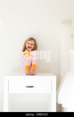 Ragazza in pigiama seduto sul comodino Foto Stock