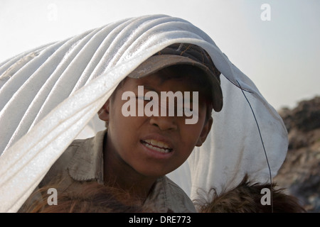 Un giovane bambino operaio boy è lo stesso di ombreggiatura dal sole caldo al tossico Stung Meanchey discarica in Phnom Penh Cambogia. Foto Stock