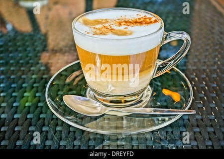 Fresche fatte cappuccino caffè in un bicchiere di vetro. Una ragazza sta riflettendo in glas tavolo. La foto è stata scattata in HDR Foto Stock