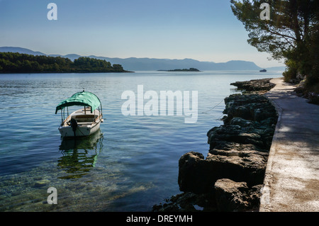 Piccola barca da pesca con bimini. ancoraggio in acque poco profonde vicino alla costa rocciosa. Un sentiero conduce all'orizzonte Foto Stock