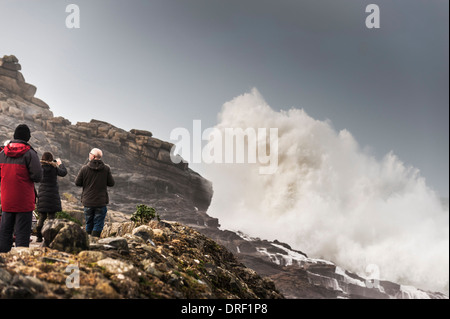 I turisti guarda come molto grandi onde crash su rocce di Sennen Cove in Cornovaglia. Foto Stock